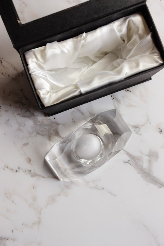 A vintage Rosenthal crystal votive rests on a marble surface beside an open black gift box lined with white satin.