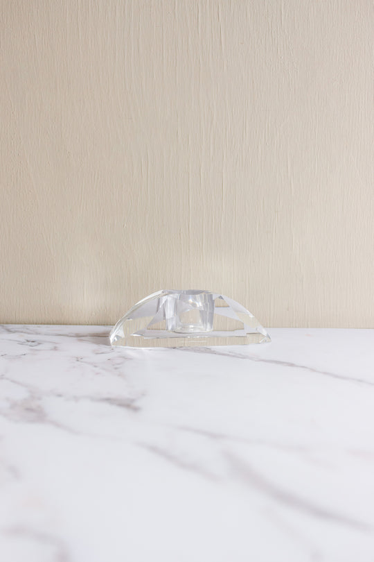 A vintage Rosenthal crystal votive, small and transparent with geometric facets, rests on a white marble surface against a beige textured wall, evoking the brand's refined elegance.
