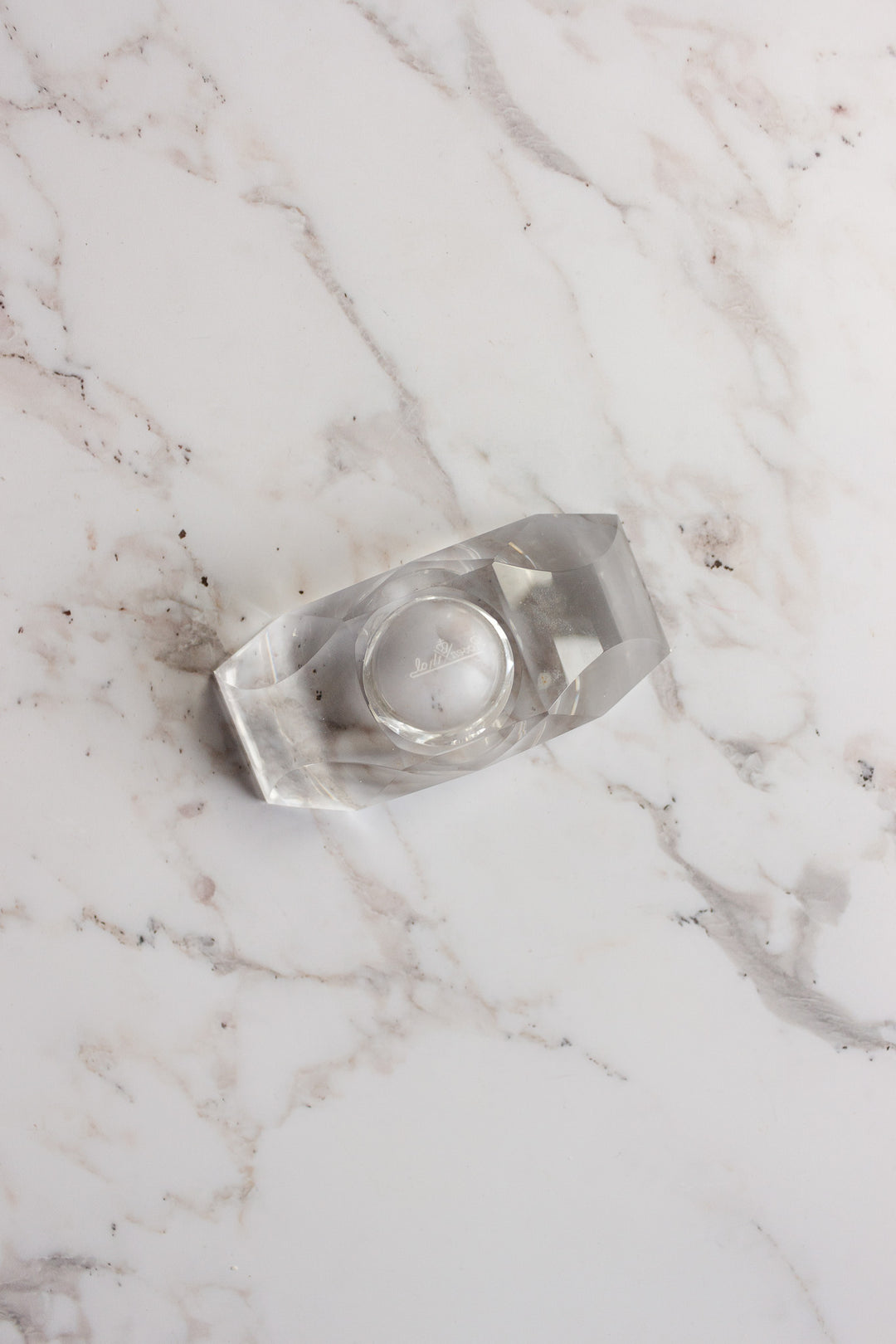 A clear tape dispenser with a roll of transparent tape sits on a white marble surface with gray veins, beside a vintage Rosenthal crystal votive.