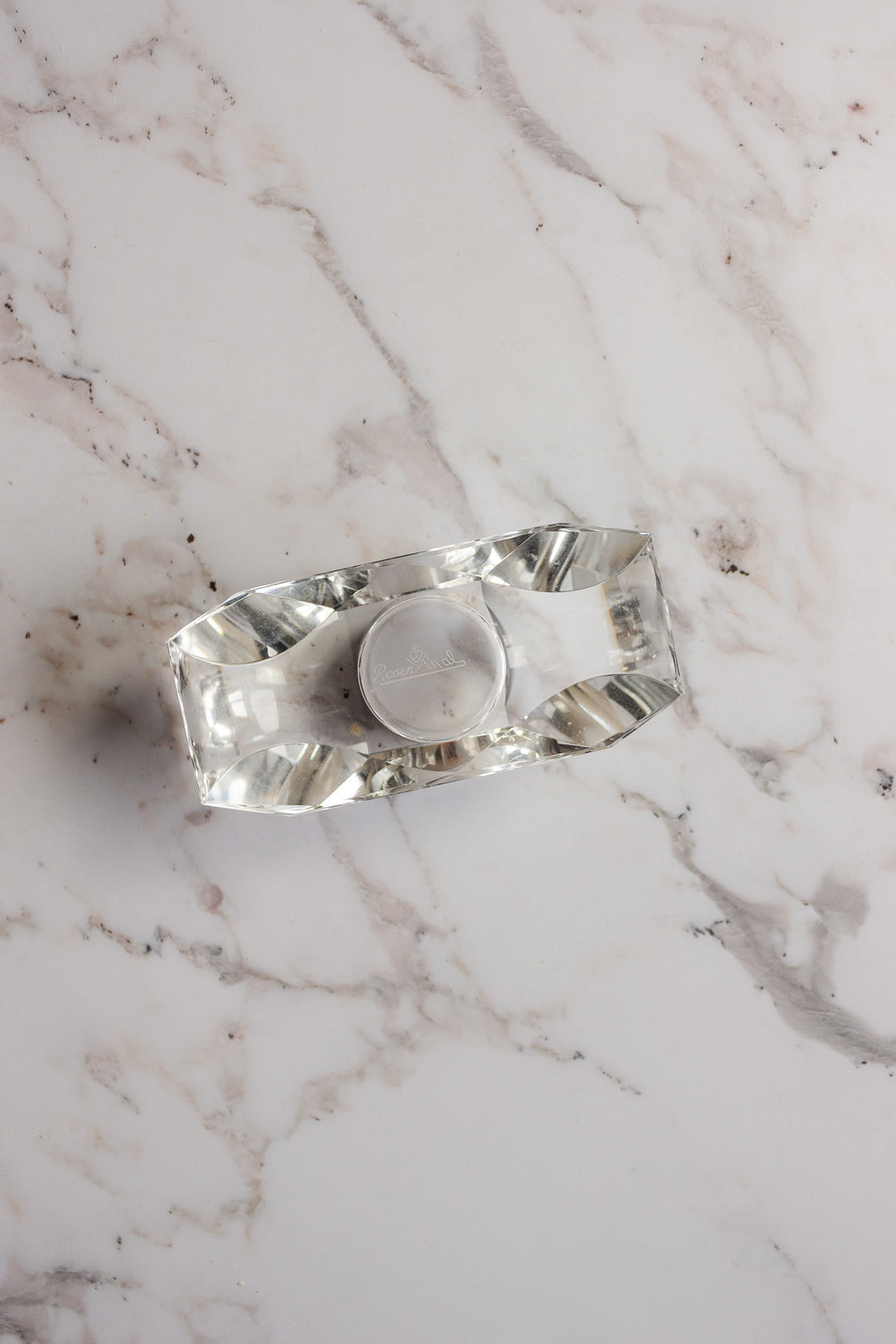 A vintage Rosenthal crystal votive holds a small round tealight on a white marble surface with grey veins, bringing understated elegance.