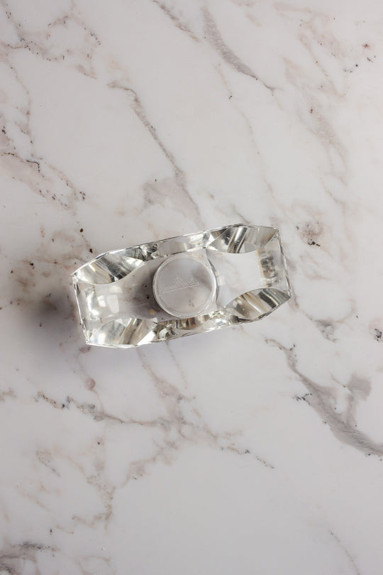 A vintage Rosenthal crystal votive holds a small round tealight on a white marble surface with grey veins, bringing understated elegance.