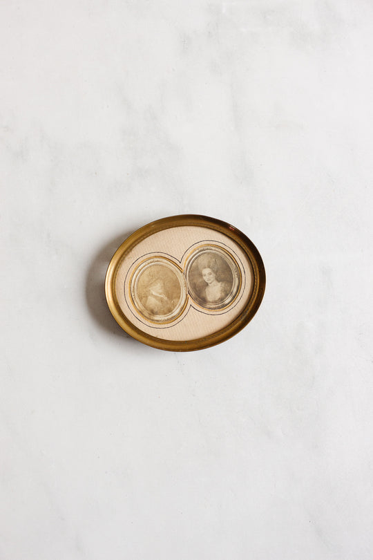 A 1920s French petite double portrait frame with French matting displays two sepia-toned vintage portrait photos side by side on a textured surface, creating a connected image within the antique brass frame.