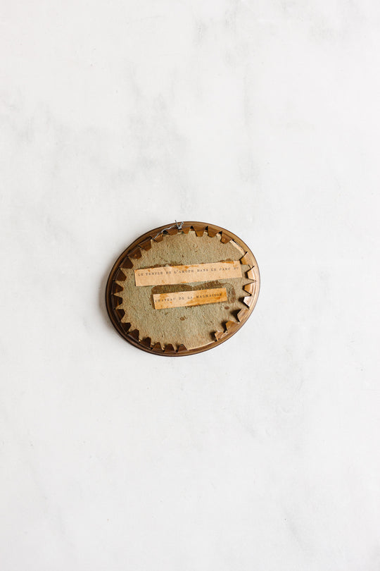 A 1920s French petite double portrait frame with French matting, oval-shaped with fabric backing and brown zigzag trim, displays two narrow strips of faded typewritten text and hangs on a white wall.