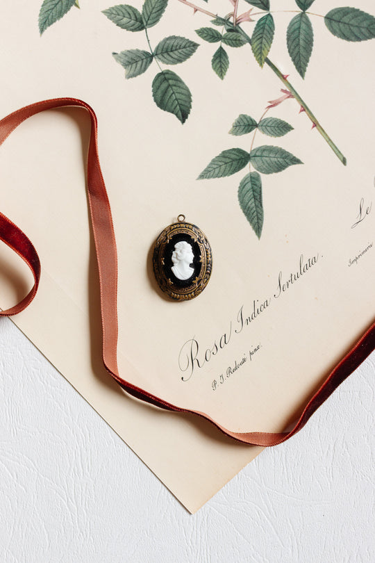 An antique French onyx inlay cameo locket rests elegantly on a piece of paper, evoking the charm of estate Aix-en-Provence.