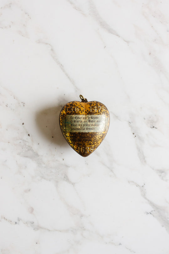 A rare antique French Coeur de Marie, Boulogne 1938 necklace with gold detailing and French engraving rests elegantly on a white marble surface.