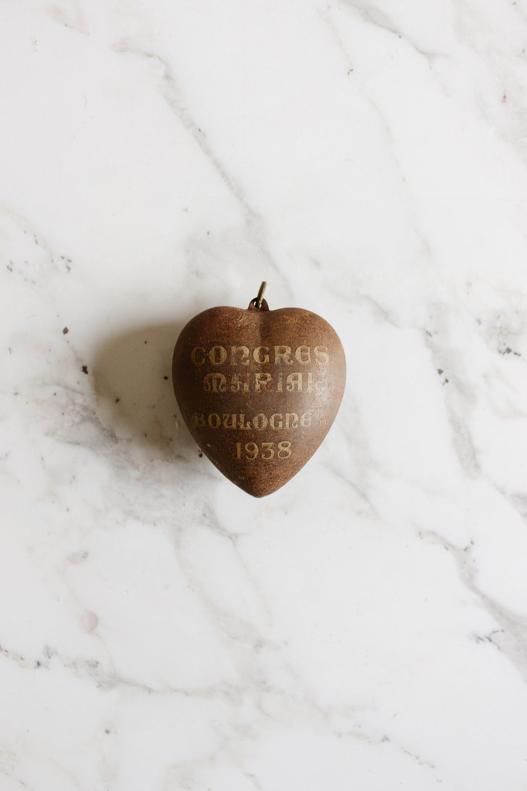 A rare antique French Coeur de Marie pendant from Boulogne 1938, with faded text, rests on white marble, evoking a cherished religious keepsake.