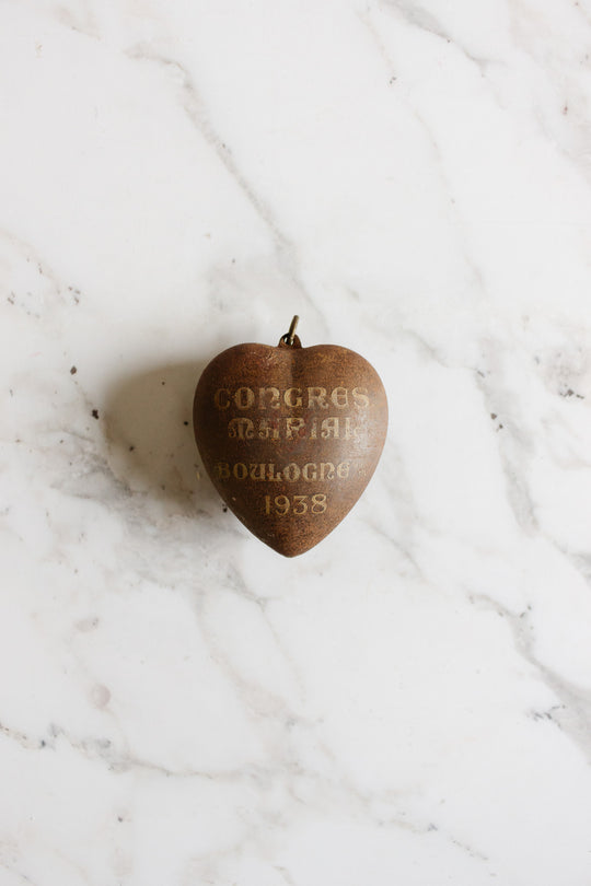 A rare antique French Coeur de Marie pendant from Boulogne 1938, with faded text, rests on white marble, evoking a cherished religious keepsake.