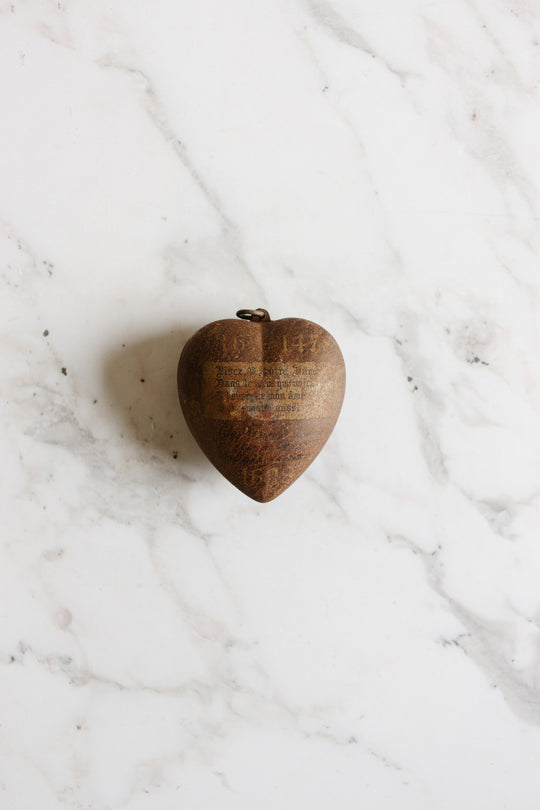 A rare antique French "coeur de marie" heart pendant from Boulogne, 1938, in brown rests on a white marble surface with light gray veins.