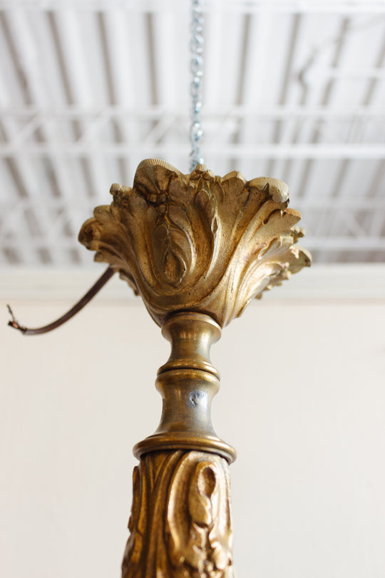 Close-up of a 1920s French brass chinoiserie 3 light chandelier with an ornate gold-colored body, suspended from a chain against a white ceiling with exposed beams.