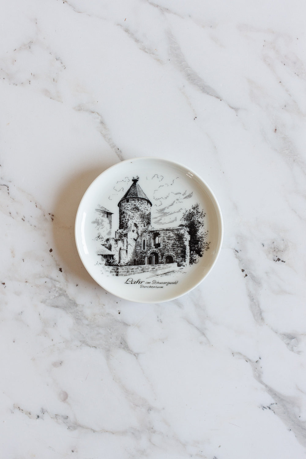 A small white vintage Kaiser Germany porcelain plate with a black illustration of a historic stone building and trees, placed on marble. This charming souvenir catch all features text beneath the image—perfect for your home.