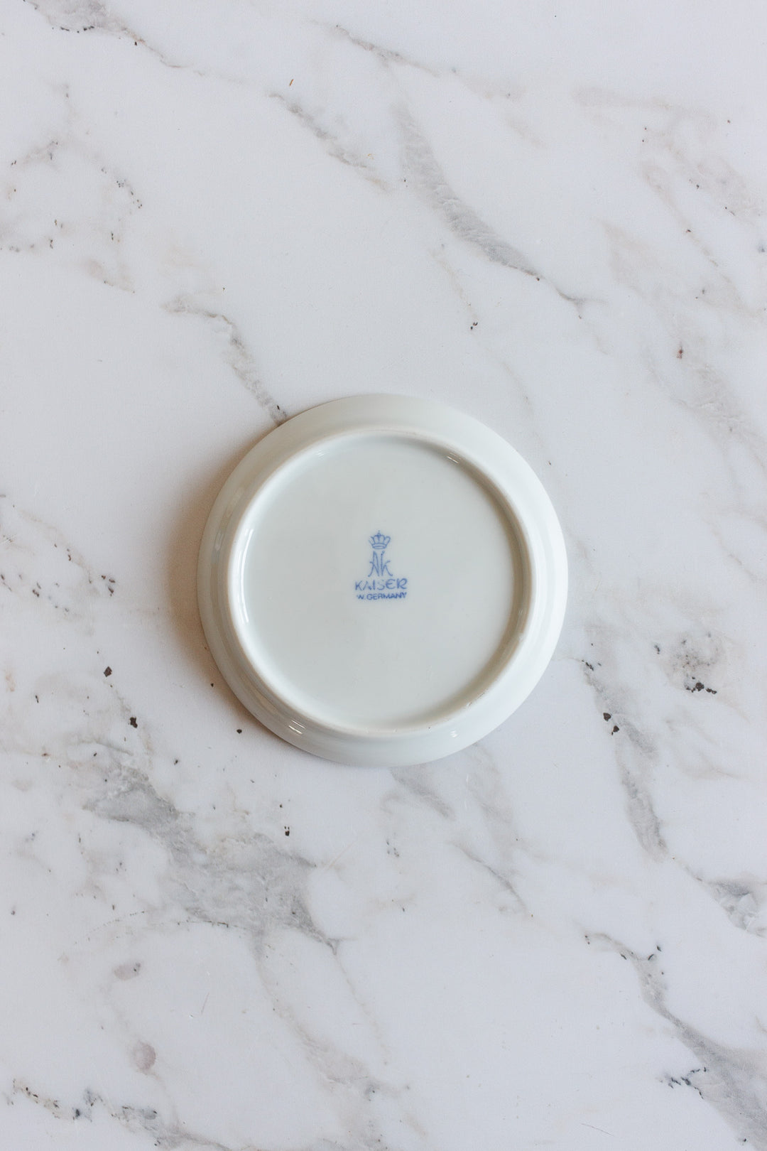 The image shows the underside of a vintage Kaiser Germany porcelain souvenir catch all with a blue crowned Kaiser W. Germany mark at the center, displayed on a white marble surface.