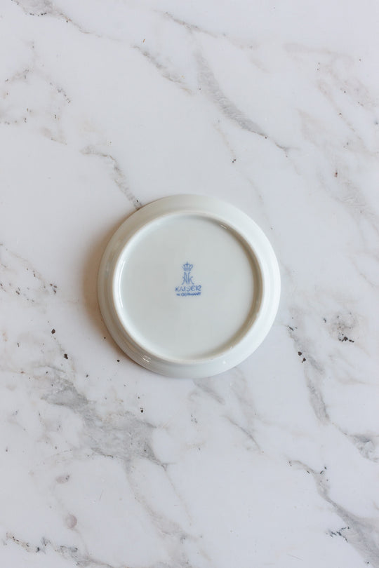 The image shows the underside of a vintage Kaiser Germany porcelain souvenir catch all with a blue crowned Kaiser W. Germany mark at the center, displayed on a white marble surface.