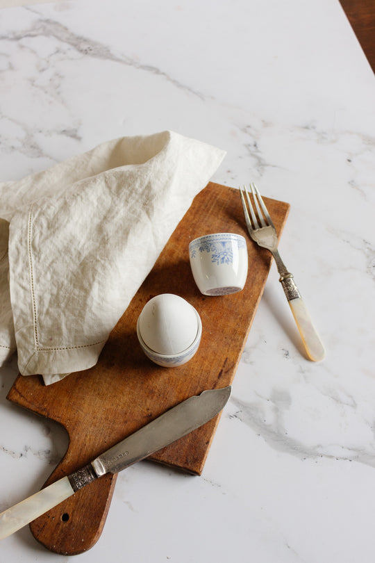 A pair of rare antique Burleigh Asiatic Pheasants egg cups sits beside a wooden cutting board with a fork and knife, bringing vintage charm to your table.