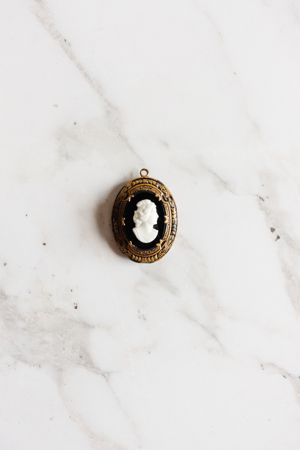 An antique French onyx inlay cameo locket with a white woman’s profile is displayed on a white marble surface.