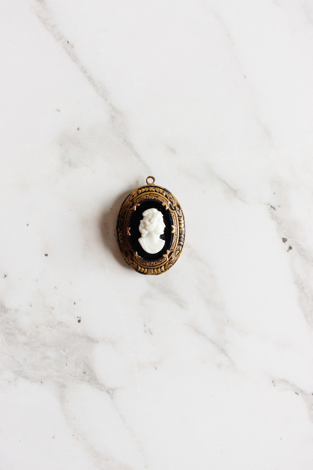 An antique French onyx inlay cameo locket with a white woman’s profile is displayed on a white marble surface.