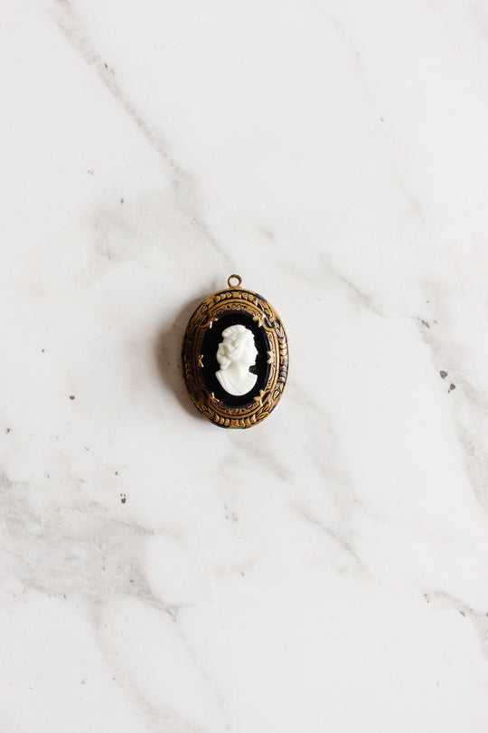 An antique French onyx inlay cameo locket with a white woman’s profile is displayed on a white marble surface.