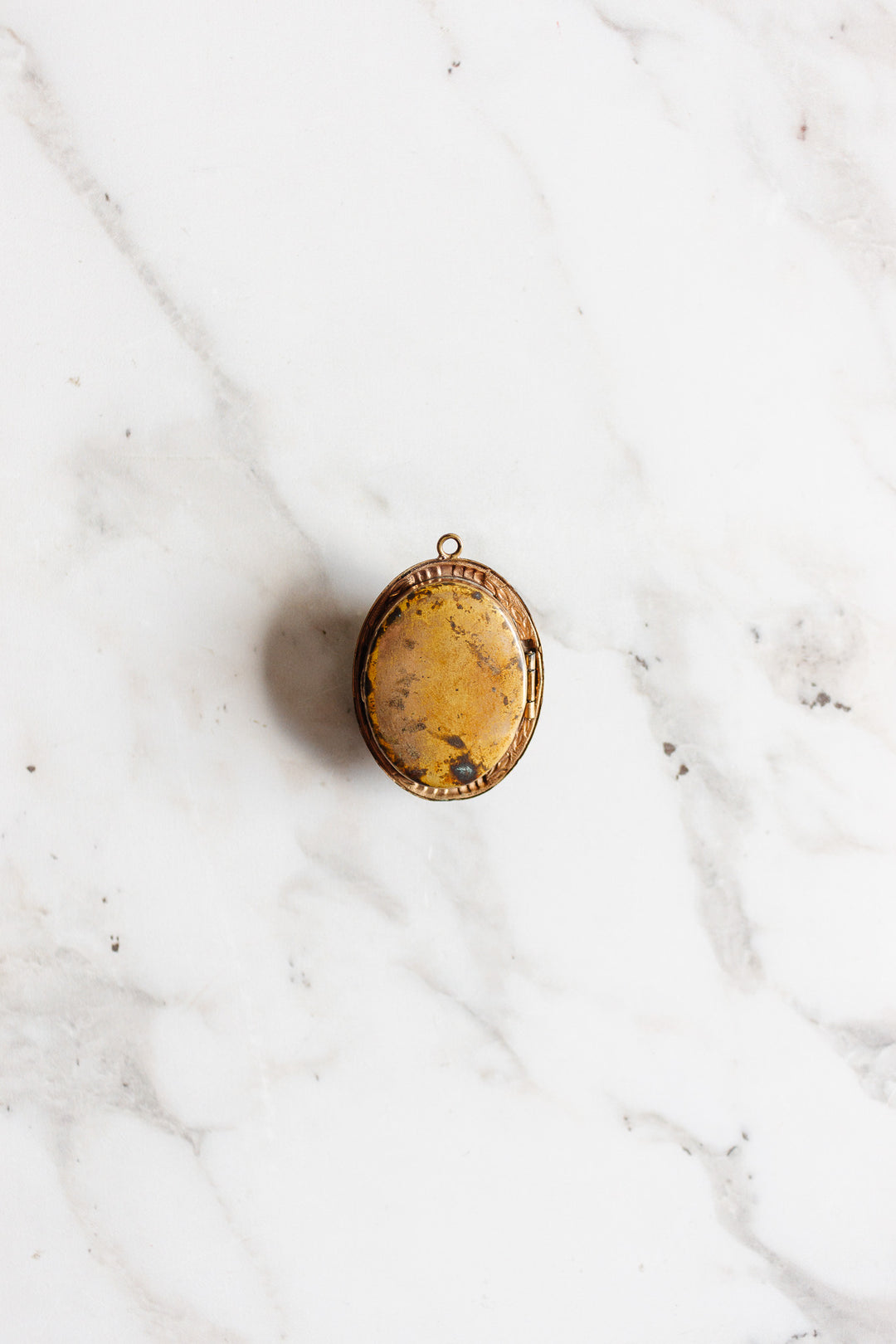 An antique French onyx inlay cameo locket with a vintage gold finish rests on a white marble background, evoking the charm of classic estate jewelry.