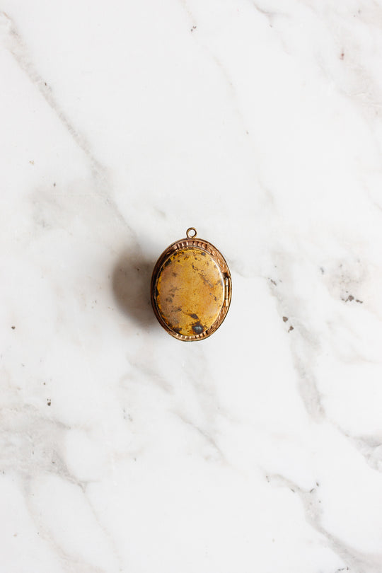 An antique French onyx inlay cameo locket with a vintage gold finish rests on a white marble background, evoking the charm of classic estate jewelry.