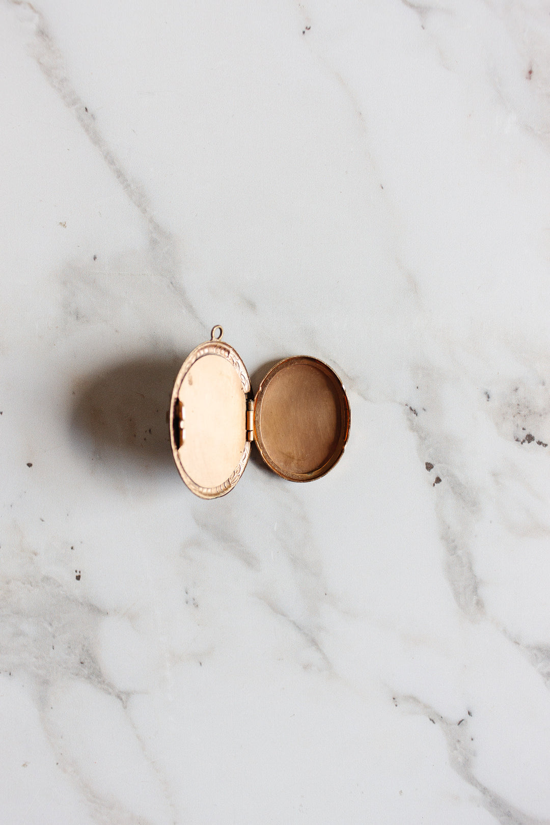An antique French onyx inlay cameo locket rests open on white marble, evoking vintage elegance. One side features a mirror, while the other contains a beige powder, suggesting it once held makeup.