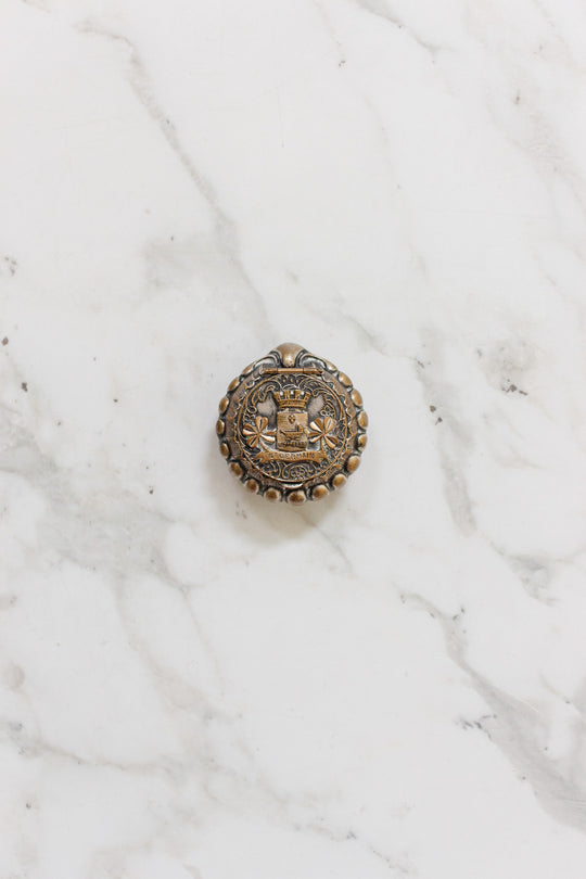 The antique French "St. Germain" pill box, a round metal object, rests elegantly on a marble surface.