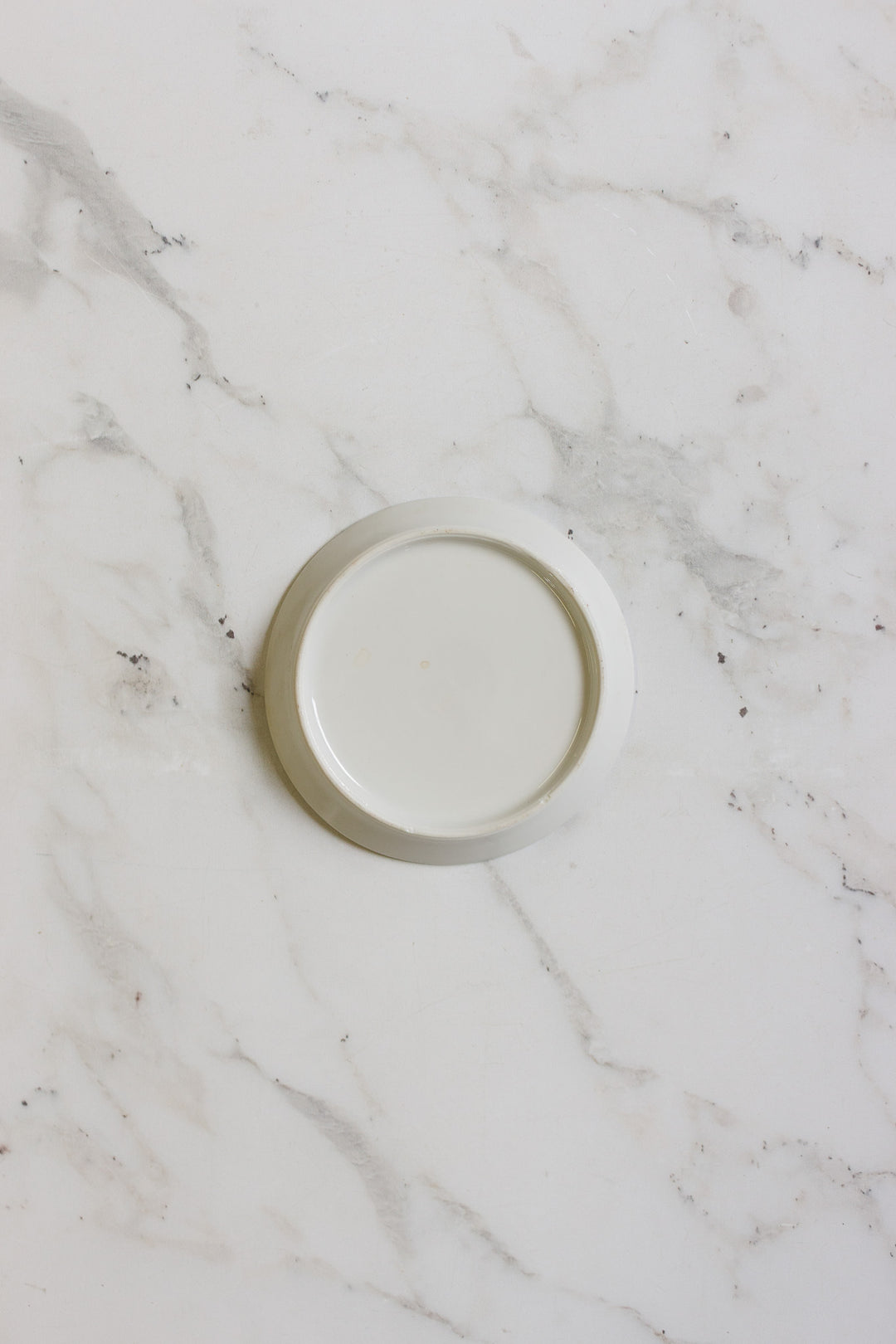 A german coasters set, featuring a plain white minimalist design, sits centered on a white marble surface with gray veining. The coasters appear clean and empty.