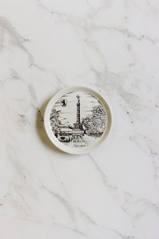 A german coaster with a black and white illustration of Berlin landmarks, including the Victory Column and a car, is displayed on a marble surface.