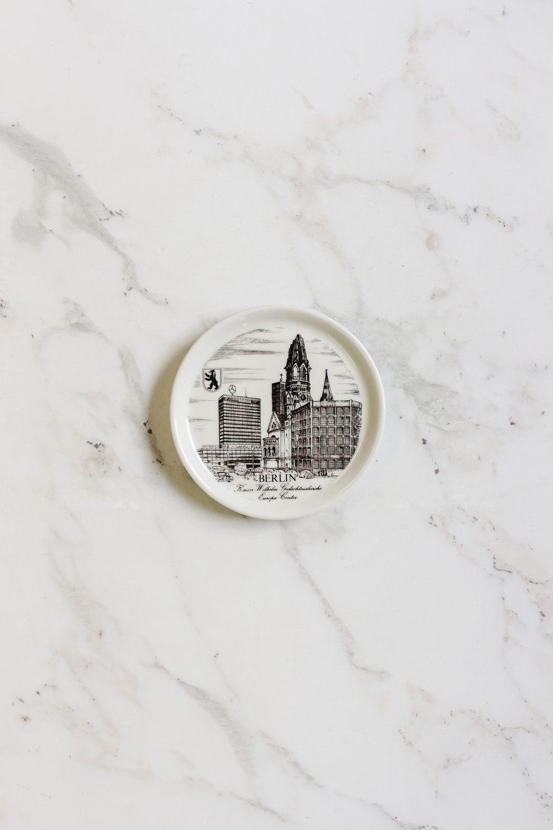 A set of german coasters, each small, round, and white, with black illustrations of Berlin landmarks and the bear emblem, displayed on a white marble surface.