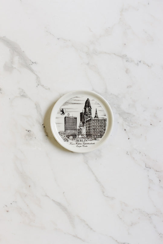 A set of german coasters, each small, round, and white, with black illustrations of Berlin landmarks and the bear emblem, displayed on a white marble surface.