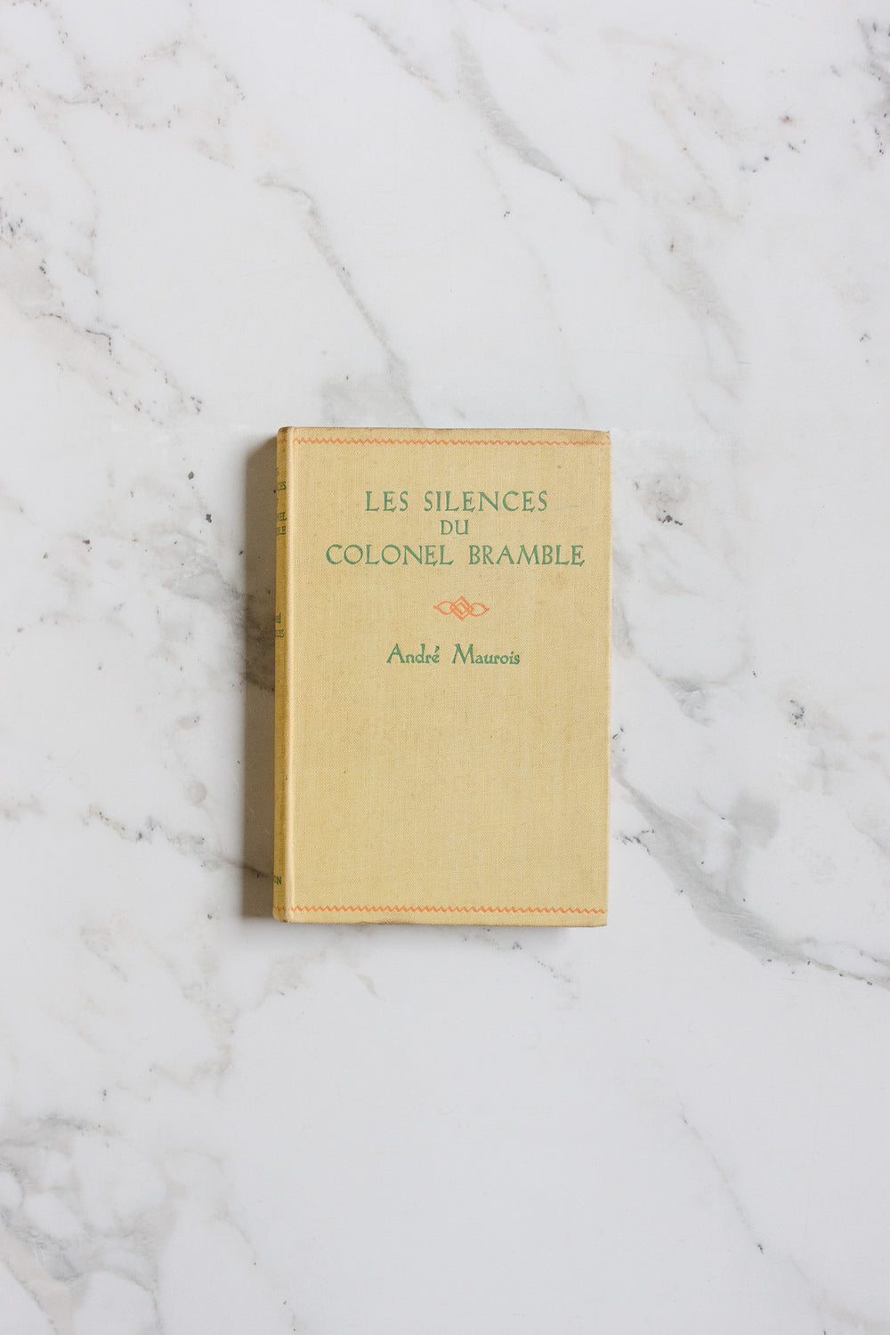 A beige hardcover book from the books collection rests on a white marble surface with subtle gray veins.