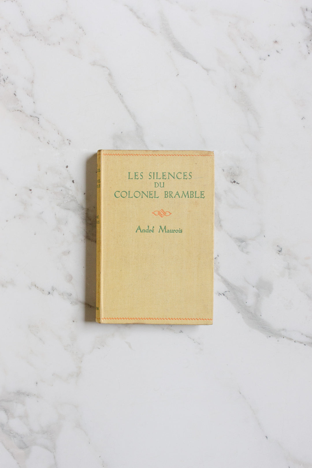 A beige hardcover book from the books collection rests on a white marble surface with subtle gray veins.
