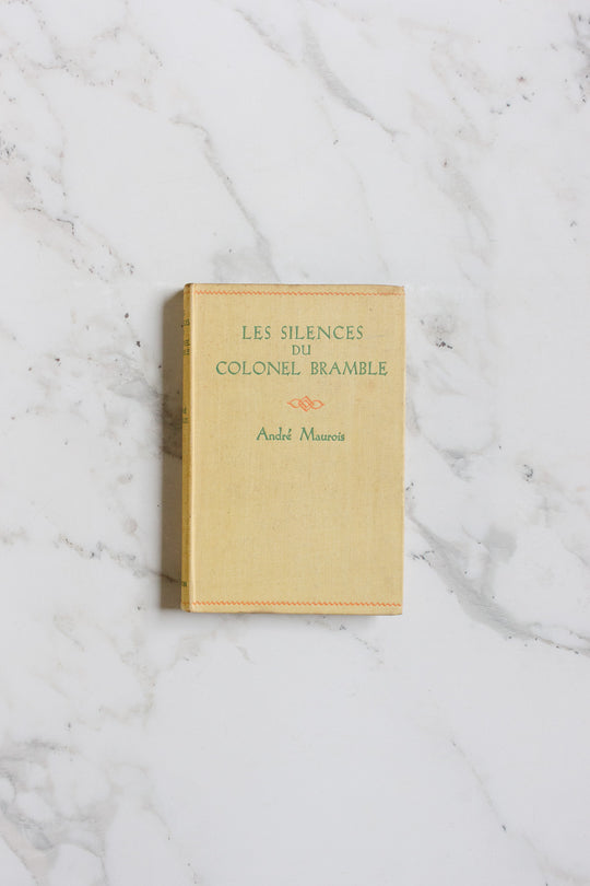 A beige hardcover book from the books collection rests on a white marble surface with subtle gray veins.