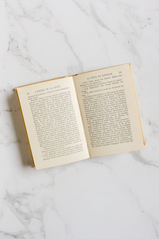 An open book from the "books" collection rests on a white marble surface, revealing French text with headings at the top of each page. The cover and exact measurements are not visible in the image.