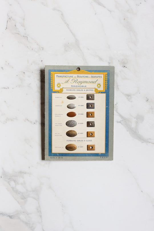 Pair of buttons ii: A vintage card featuring assorted oval and round metal buttons and fasteners labeled in French, beautifully set on a classic white marble background.