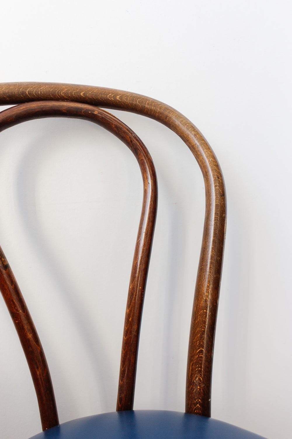 Close-up of a vintage pair of Thonet bentwood bistro chairs with curved backrests and blue cushioned seats, set against a plain white background.