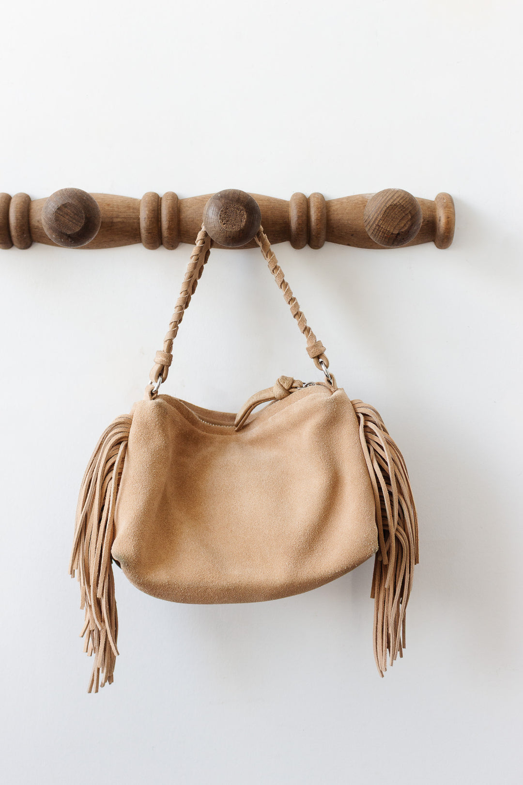 An antique French faux bamboo 4 prong patère displays a tan suede handbag with braided handles and long fringe, adding vintage charm to the crisp white background.