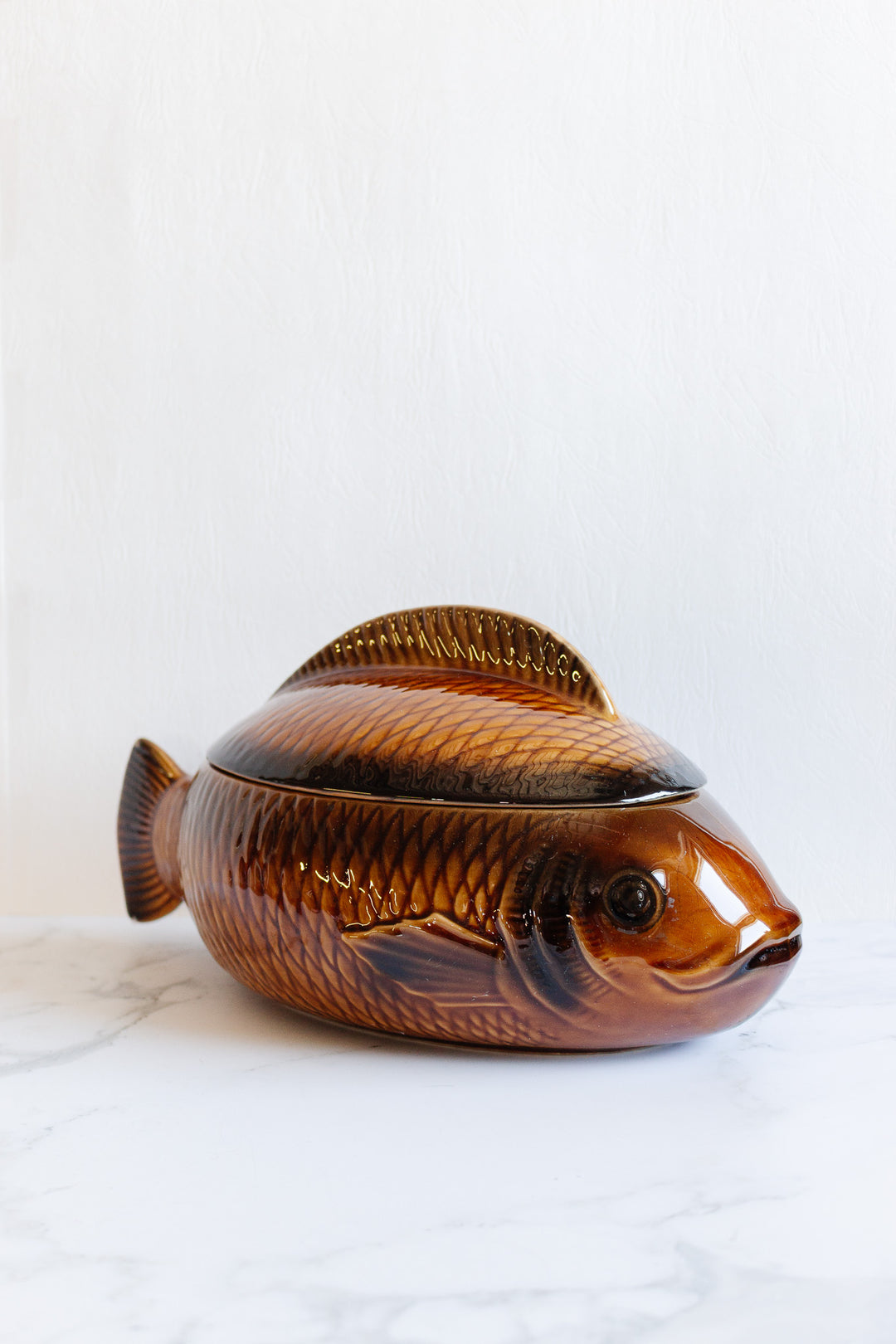 The fish soupiere is a ceramic serving dish shaped and painted like a brown fish, with a removable lid forming the top half, shown on a white surface against a light background; see details for exact dimensions.