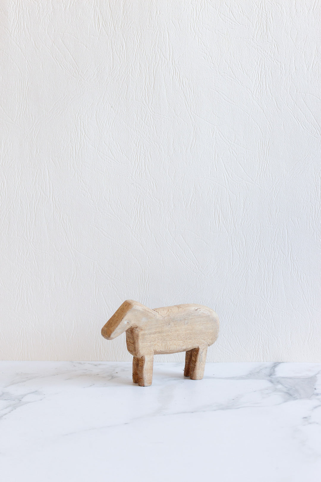 A compact wooden animals figurine stands on a white marble surface against a light textured wall background.