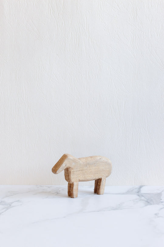 A compact wooden animals figurine stands on a white marble surface against a light textured wall background.