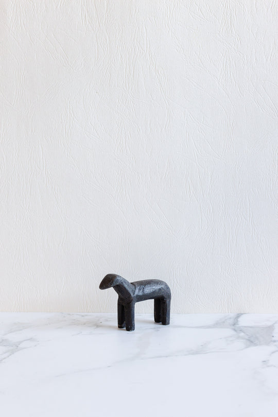 A compact, minimalist black wooden animal sculpture with four legs stands on a white marble surface against a textured white wall—its small size is perfect for modern decor.