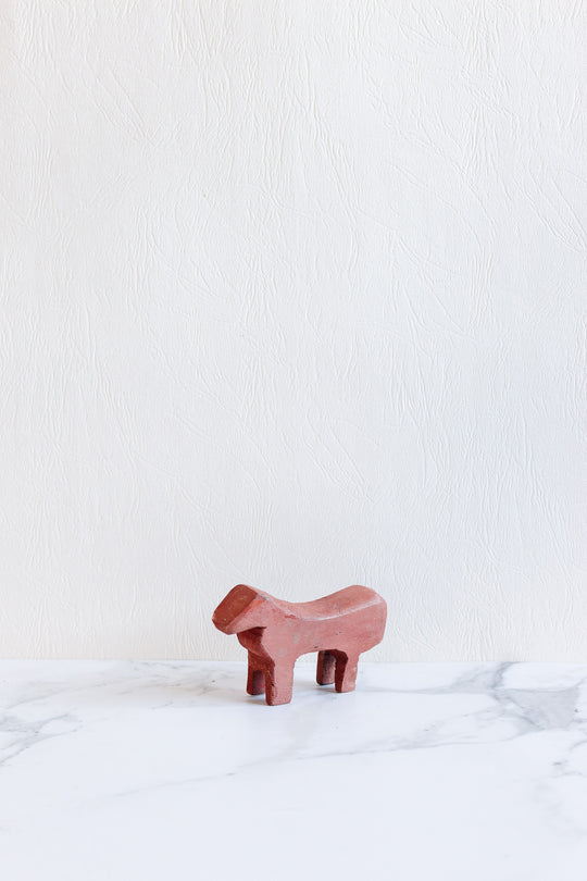 A small, minimalist wooden animals figurine in reddish-brown stands on a white marble surface against a textured light background.