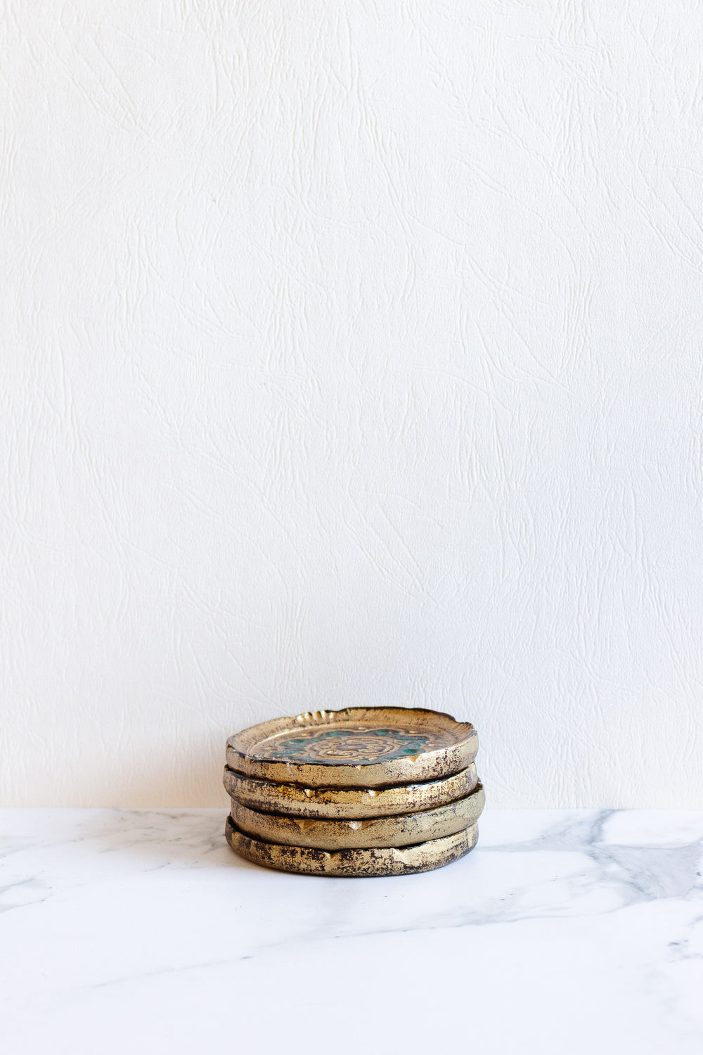 Four Florentine coasters with elegant dimensions are stacked on a white marble surface against a textured white wall background.