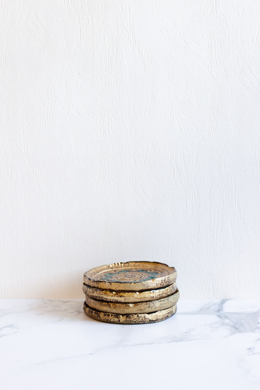Four Florentine coasters with elegant dimensions are stacked on a white marble surface against a textured white wall background.