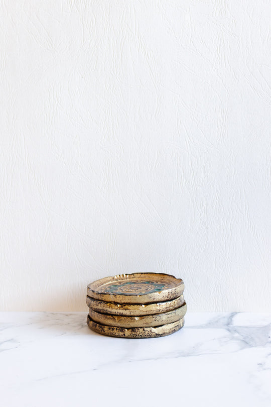 Four Florentine coasters with elegant dimensions are stacked on a white marble surface against a textured white wall background.