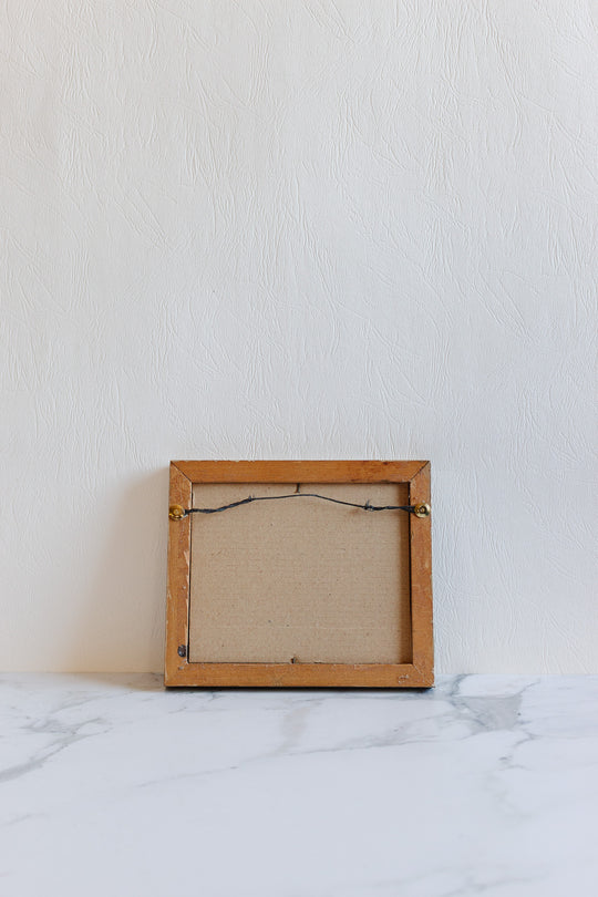 A small empty wooden art frame with visible dimensions is seen from the back, resting on a white marble surface against a textured white wall.
