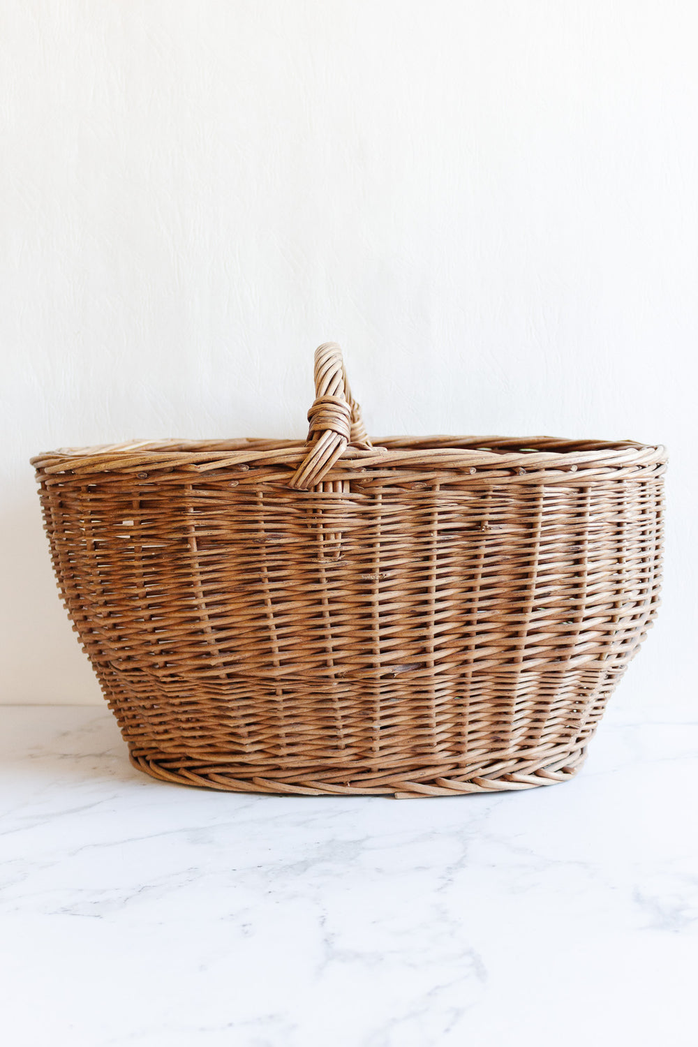A spacious, empty basket with a single handle sits on a white marble surface against a plain white background.
