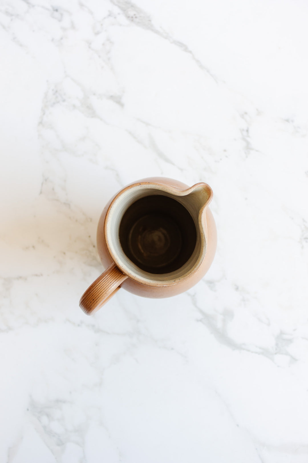 A top-down view of the large jug, an empty ceramic pitcher with a handle and spout on a white marble surface, highlights its elegant shape and dimensions.