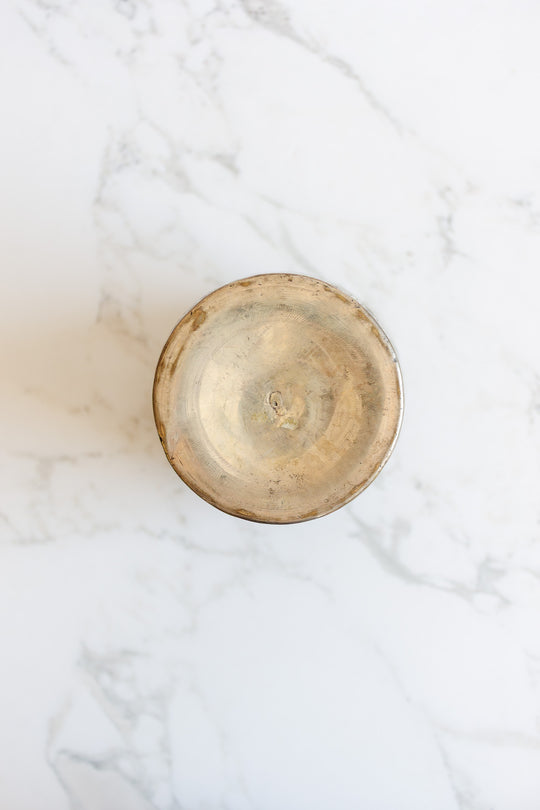 A round metal vase with a slightly tarnished finish and classic shape, photographed from above on a white marble background.
