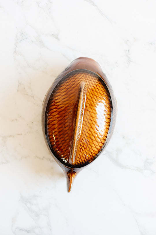 A brown, ceramic fish soupiere with a textured, scale-like lid and unique dimensions sits on a white marble surface, making it a standout decorative piece.