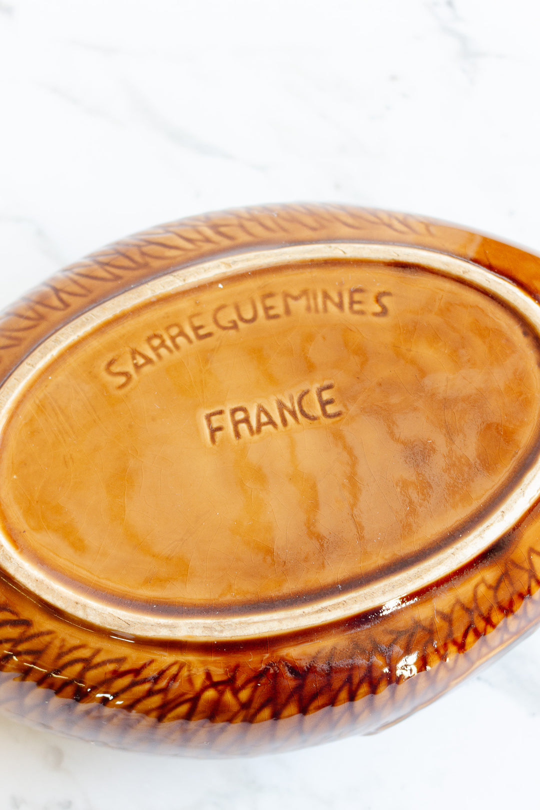 A brown ceramic fish soupiere with SARREGUEMINES FRANCE stamped on the bottom, displayed on a white marble surface; please inquire for dimensions.