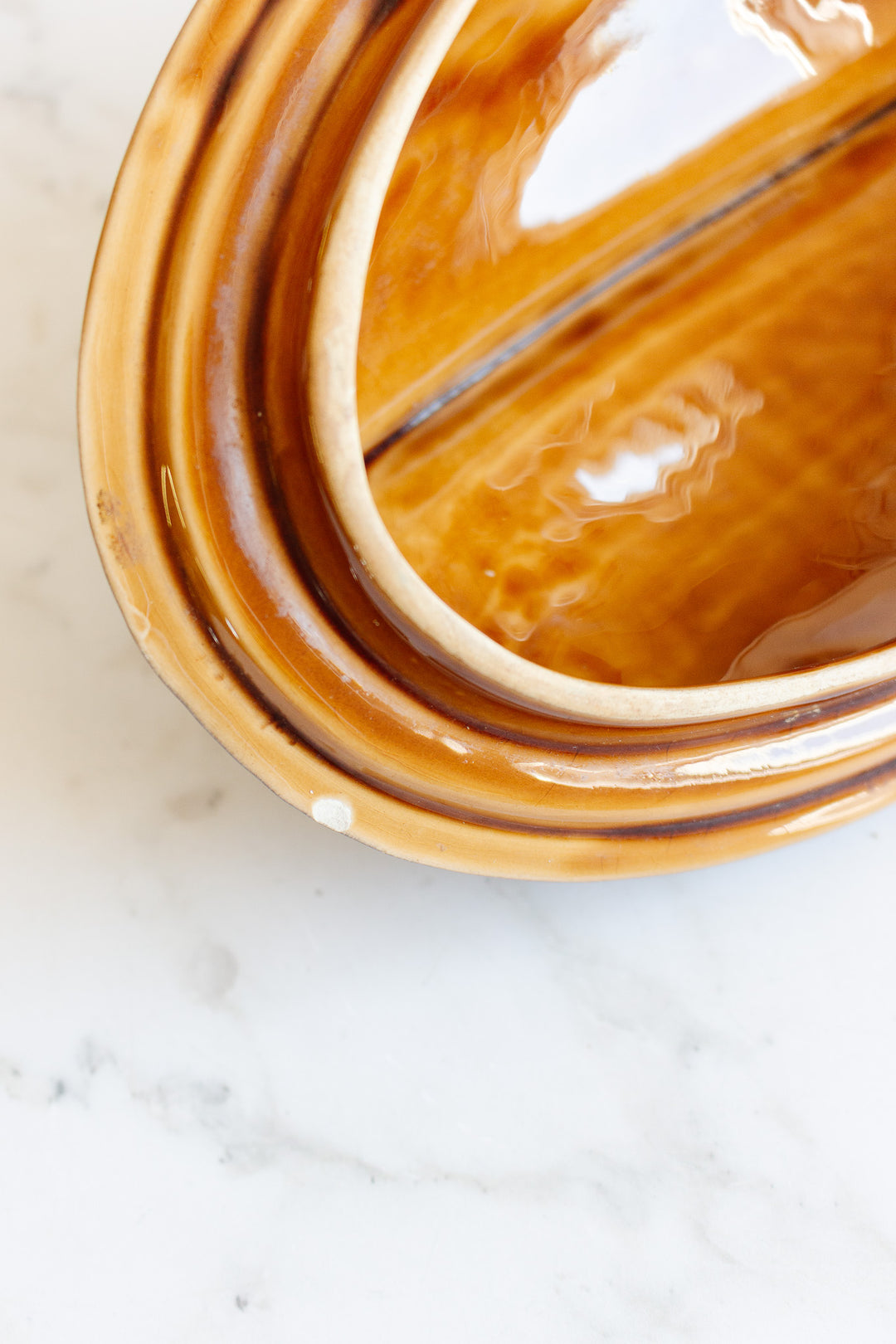 Close-up of a shiny, brown-glazed fish soupiere with a rounded edge and visible dimensions, placed on a white marble surface. The photo highlights the smooth and reflective interior of the fish soupiere.
